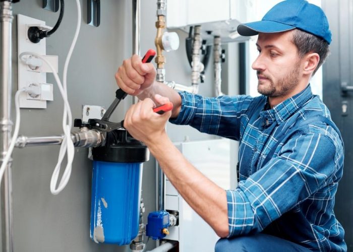 Young plumber or technician in workwear using pliers while installing or repairing system of water filtration